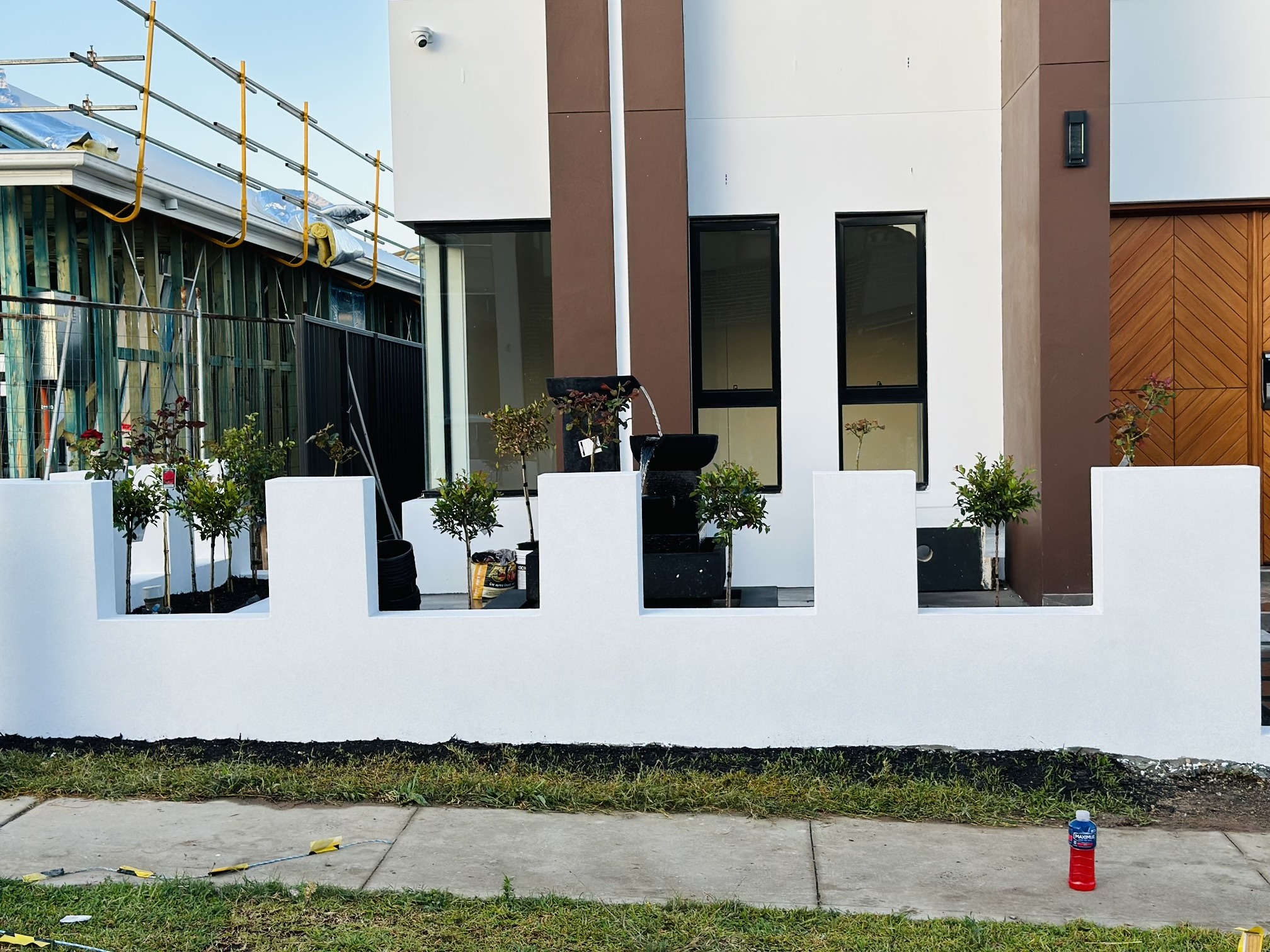 White rendered stepped front wall with planters and a black water feature in front of a new house