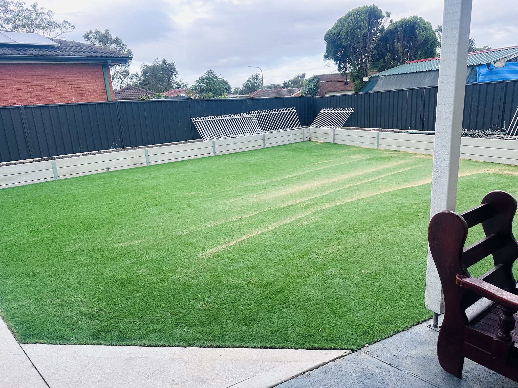 Backyard of new synthetic grass framed by a dark colorbond fence and concrete edging