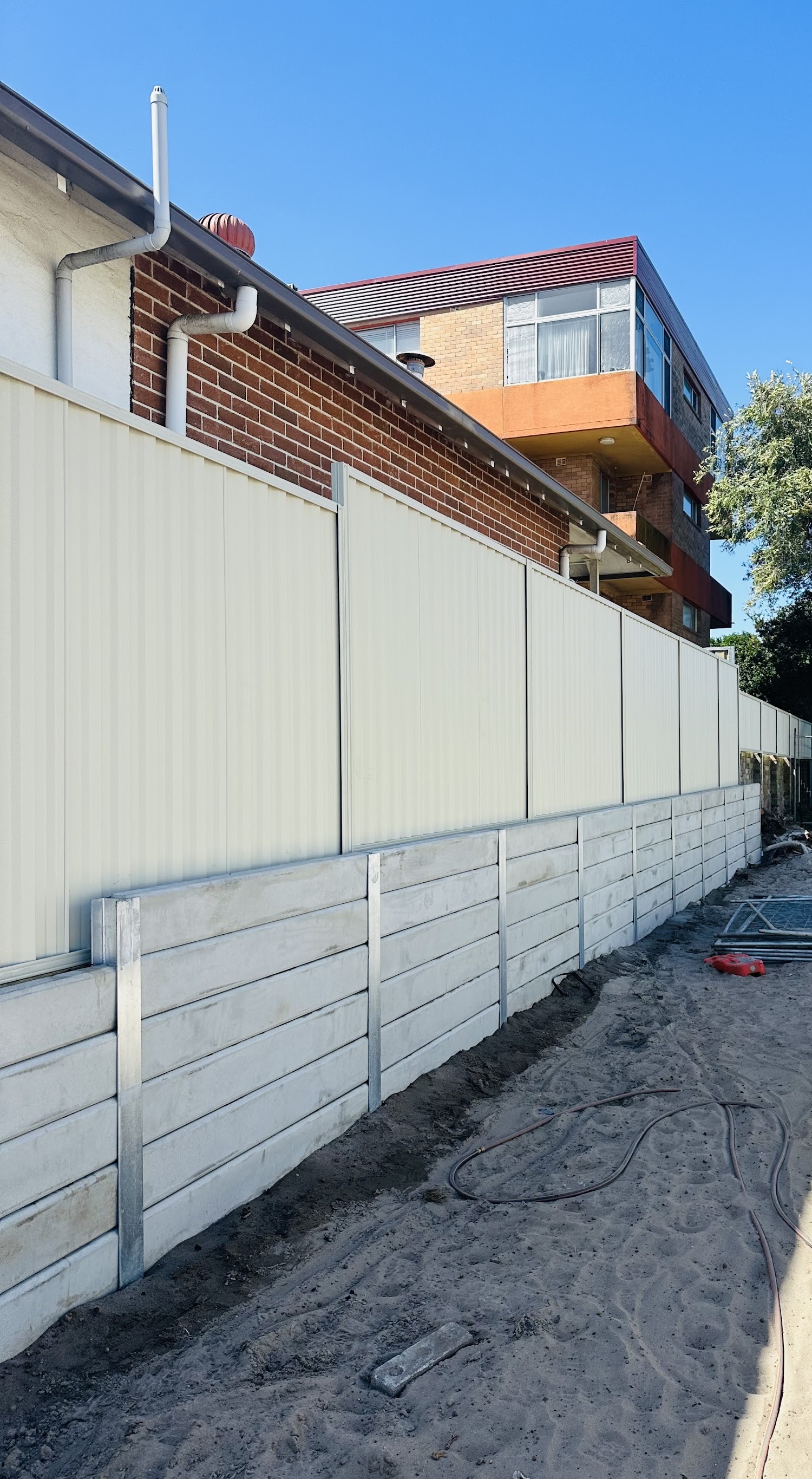 Long concrete sleeper retaining wall on galvanised posts running along a colorbond fence
