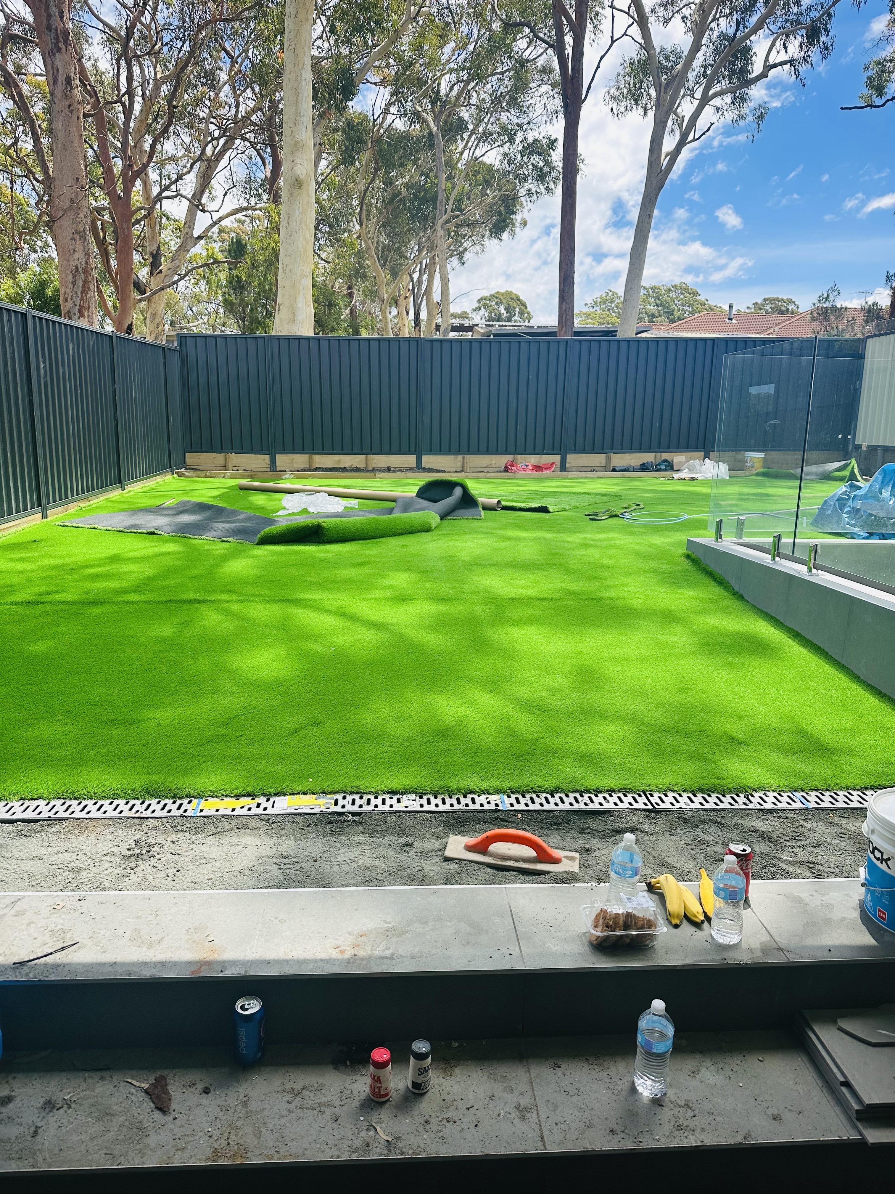 Synthetic turf being installed in a backyard, with offcuts and tools still on the lawn