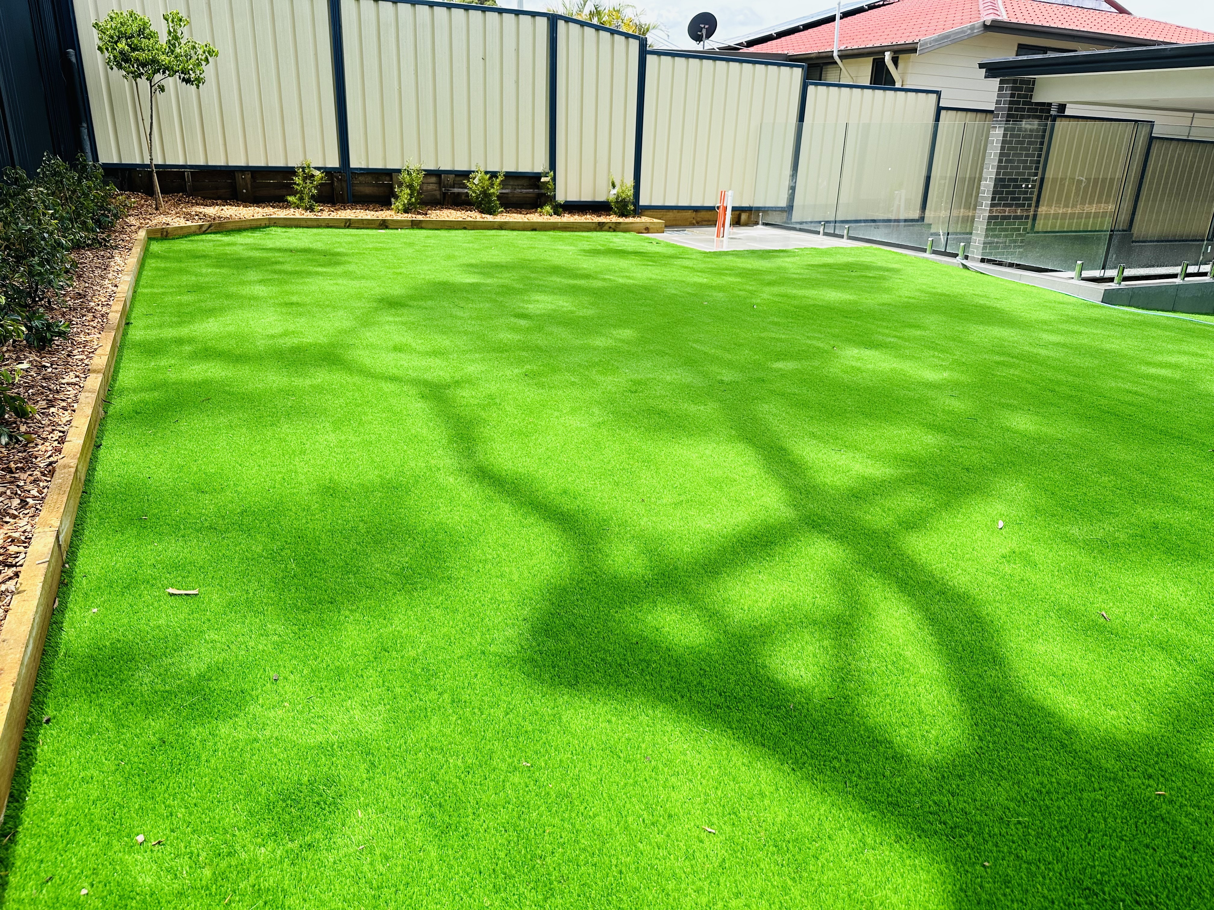 Finished bright synthetic lawn with timber edging and new garden bed along a cream fence