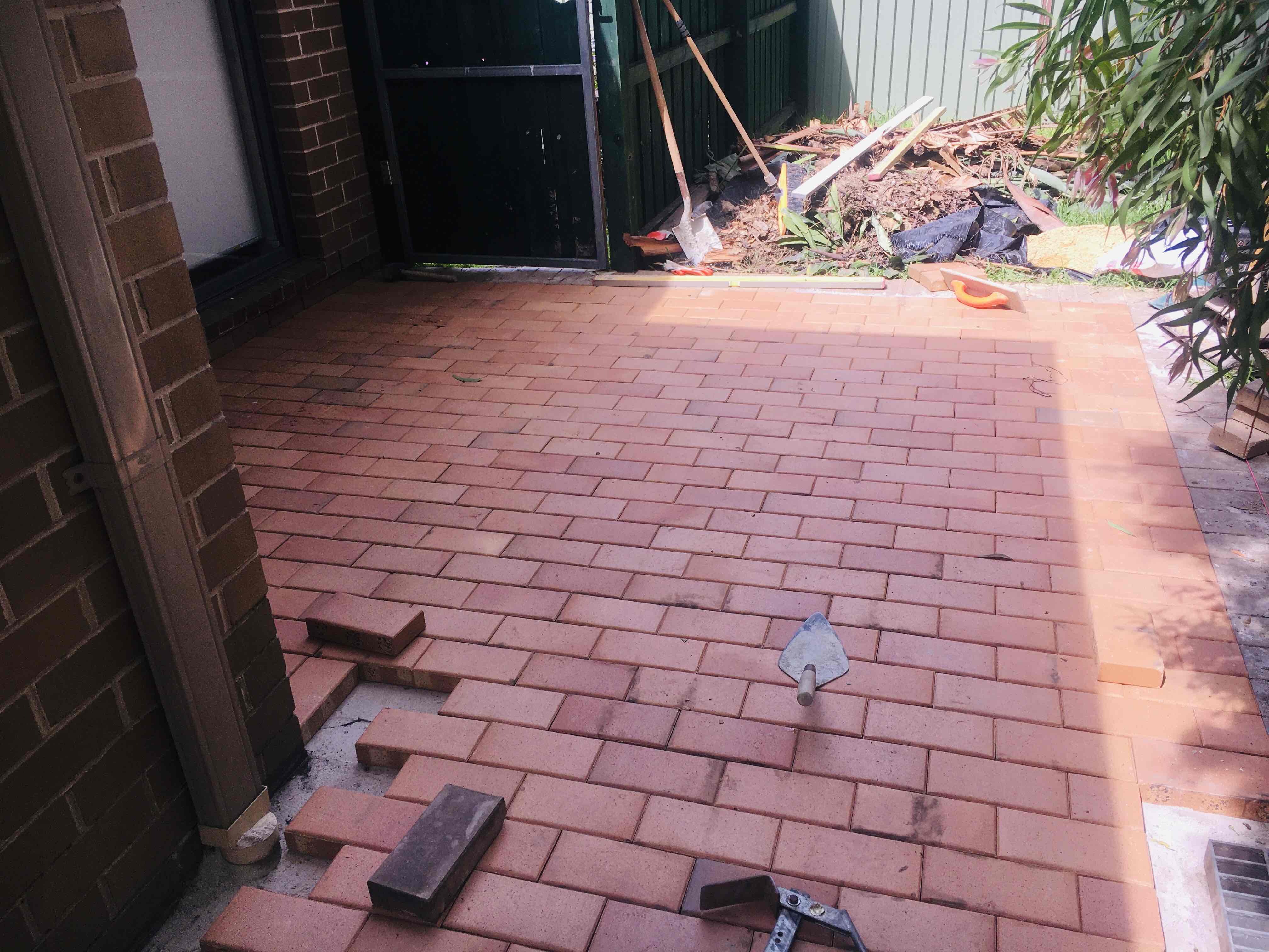 Red brick courtyard paving part-way through being laid, with a trowel on the bricks