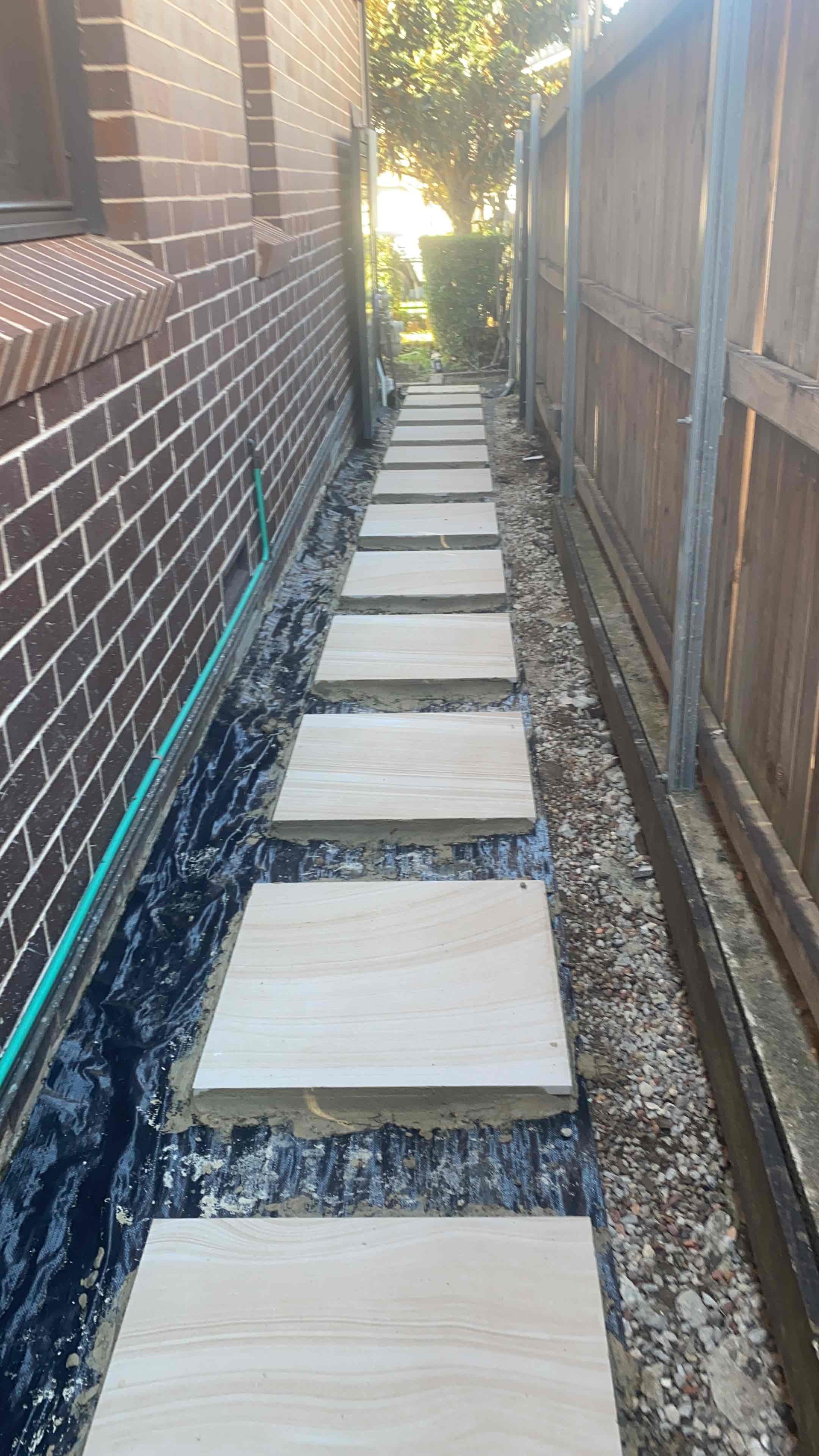 Sandstone stepping pavers laid down a narrow side passage beside a brick house