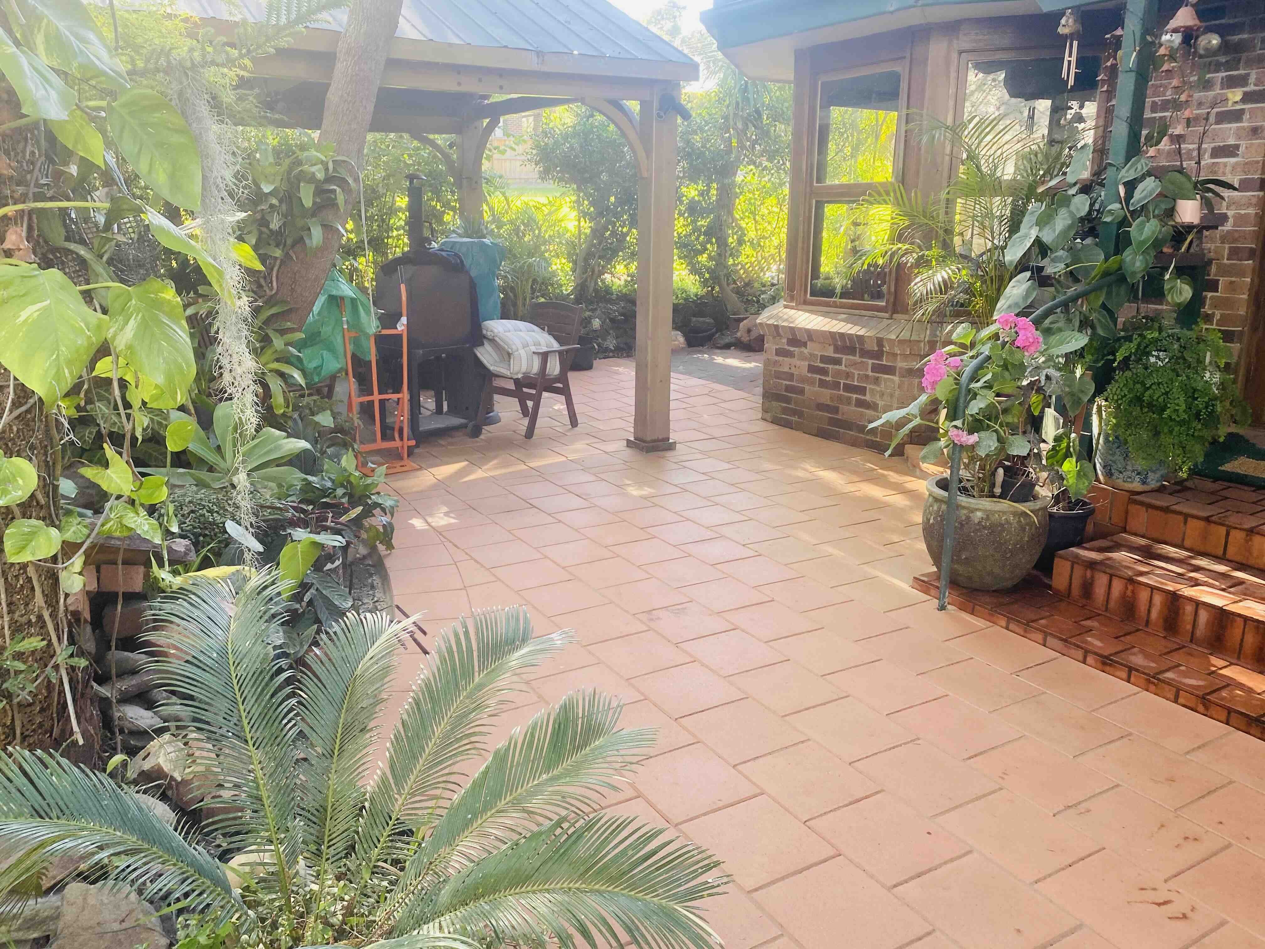 Terracotta courtyard paving winding past a timber gazebo and a cycad